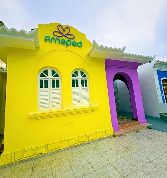 Fachada da Clínica AmePed, prédio amarelo com portal de entrada roxo, na Rua Rui Barbosa em Jacobina