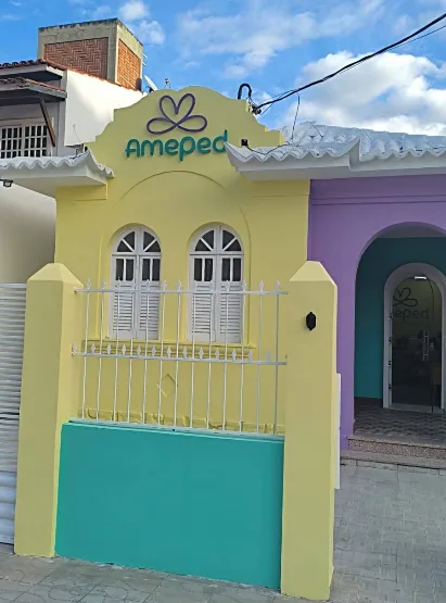 Fachada da Clínica AmePed vista em ângulo, com portal de entrada em roxo ao lado da parede amarela